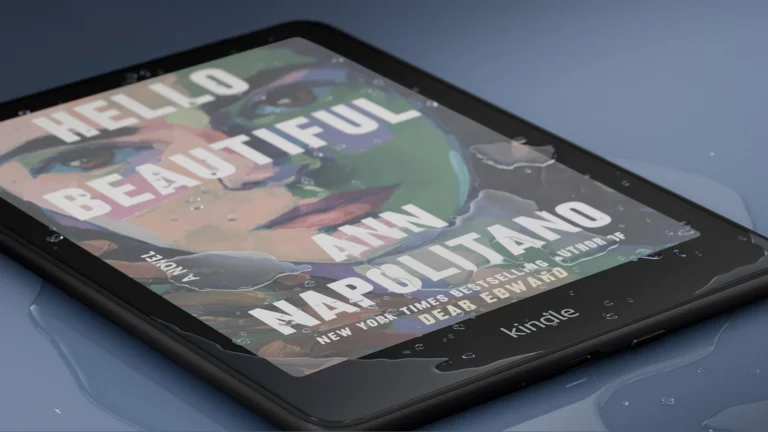 Kindle Colorsoft lying on a wet blue surface with water droplets on the screen, showing a colour book cover and the bottom edge of the black frame